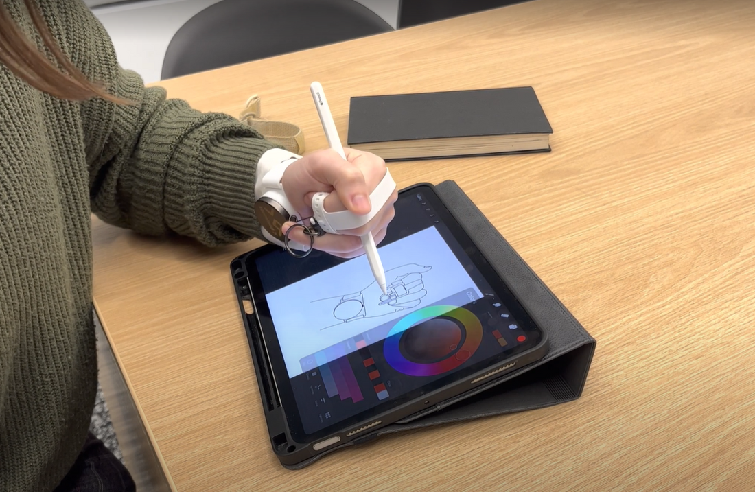 a person's hand wearing an assistive grasping tool called Fiber to help hold a stylus while they draw on a tablet